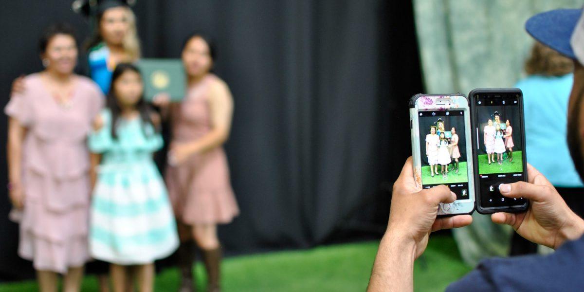 taking a picture of graduate and her family using two cell phones